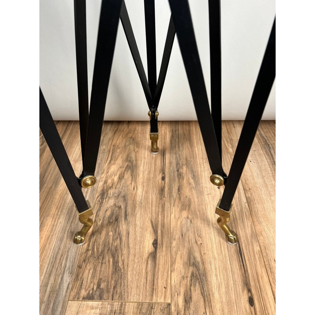 The Vintage Maison Jansen Style Marble Top Sculpture Stand features black metal legs with gold-toned feet, reminiscent of neoclassical gilt iron tables, shown on a light brown wood floor and photographed from a low angle.
