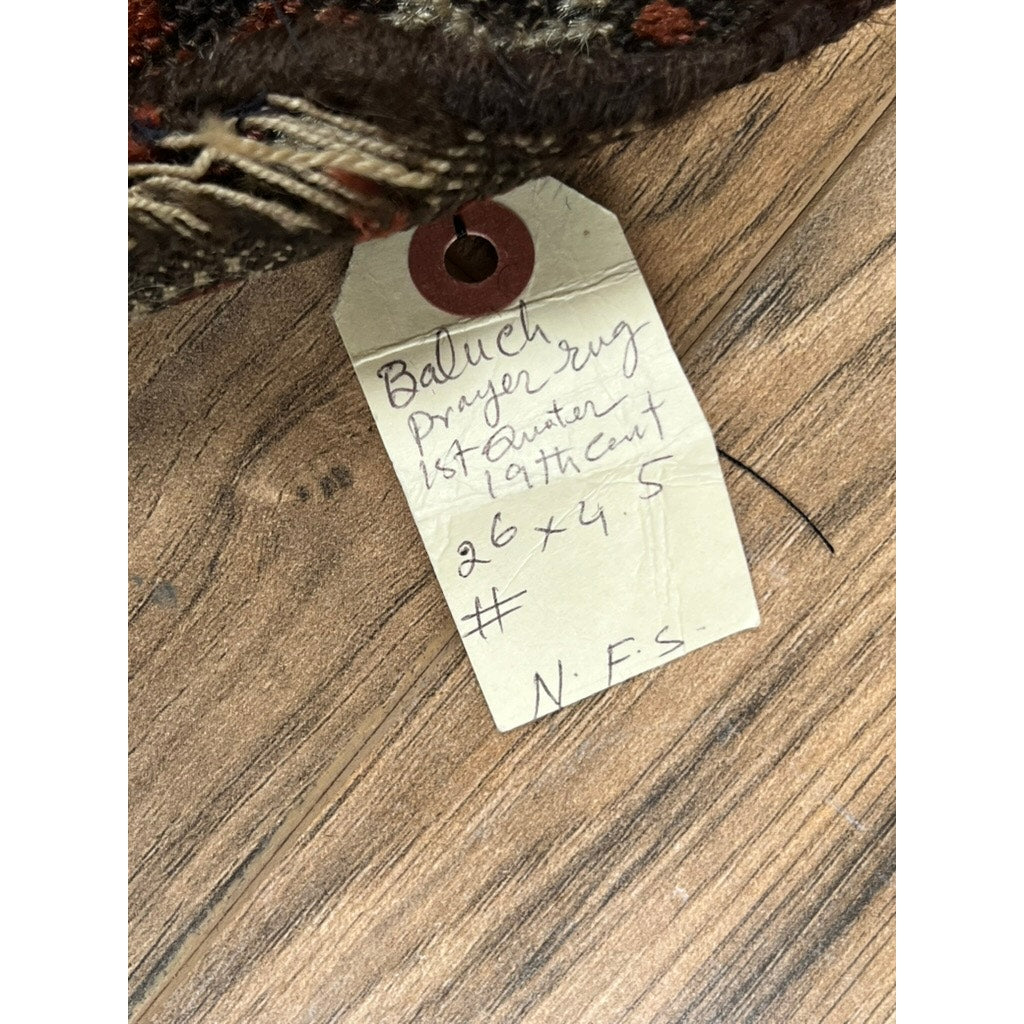 A handwritten tag on wood partially beneath this Early Antique Baluch Prayer Rug with Rare Comb Motif, Northeast Persia, c. Early 19th Century – 2’6 x 4’5 identifies the rug’s details. Brand: None/Unknown.