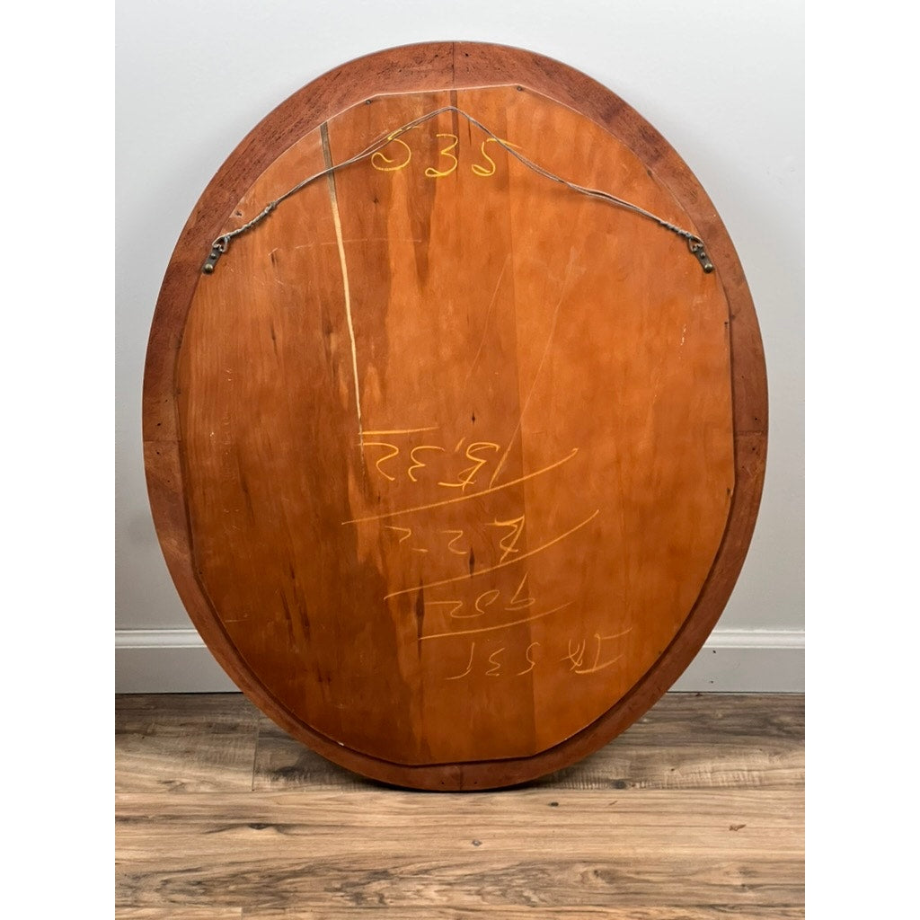 The Vintage Oval Maple Wall Mirror, brand unknown, stands upright on a wood floor against a white wall. Bright yellow chalk numbers and markings are visible on the back of this striking vintage mirror frame.