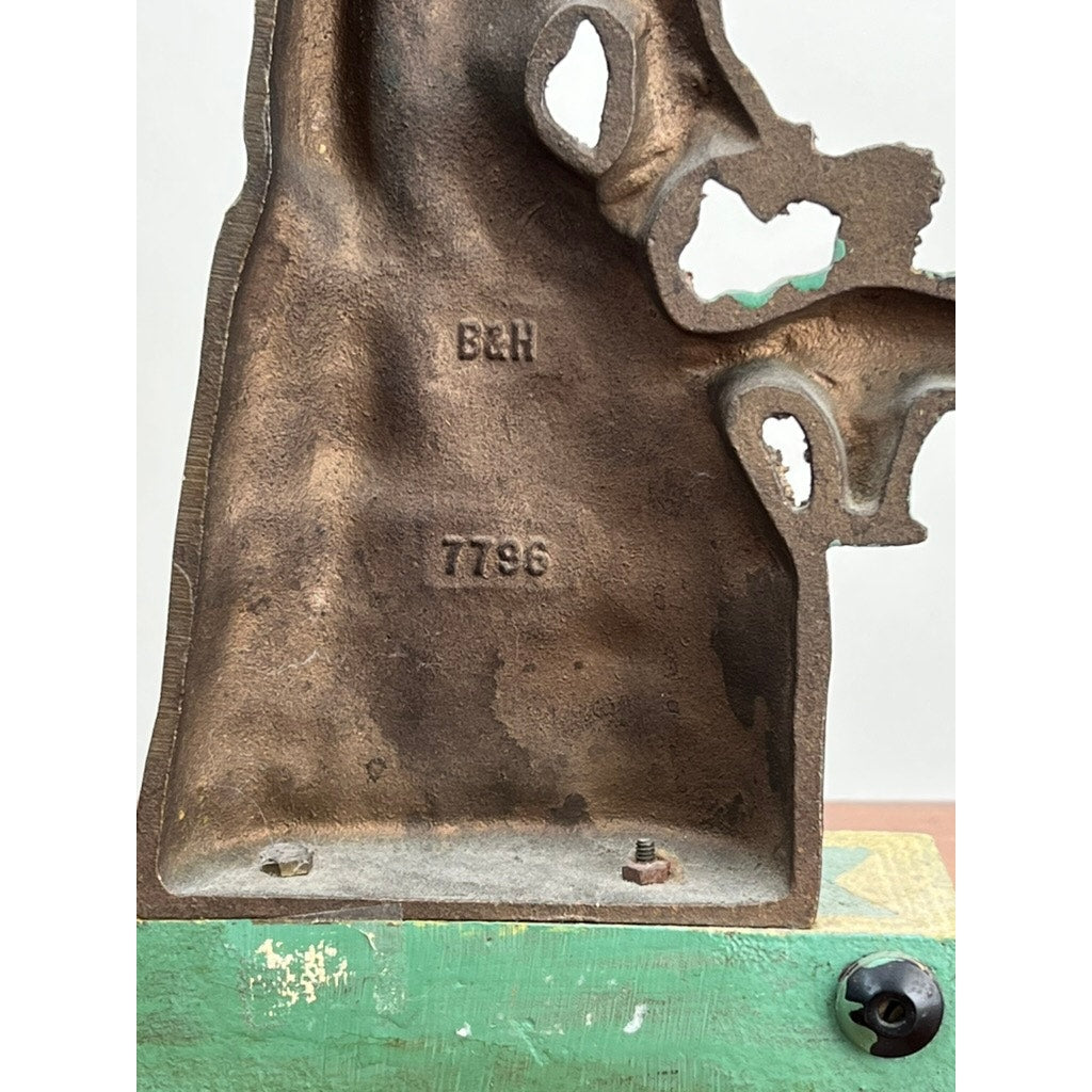 Close-up of the base of an Antique Victorian Bradley and Hubbard Woman with Flowers Door Stop, showing embossed B&H and 7796 markings, green painted edge, visible screw, and aged patina. Brand: None/Unknown.