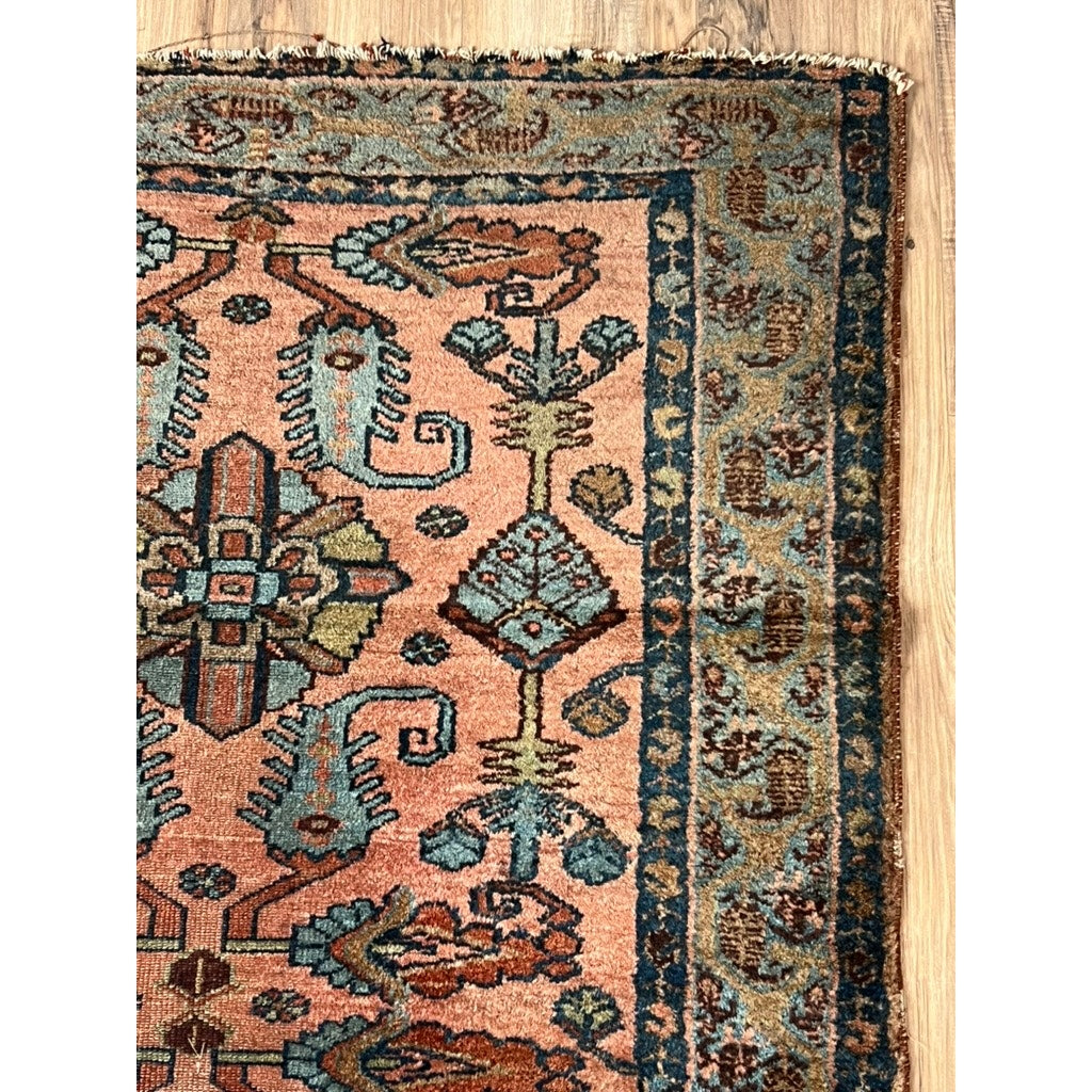 A close-up of a late 19th-century Village Rug from the Hamadan Region (3’4 x 6’9), featuring intricate blue, teal, and rust designs on a peach background with blue and tan floral borders, shown on a light wooden floor.