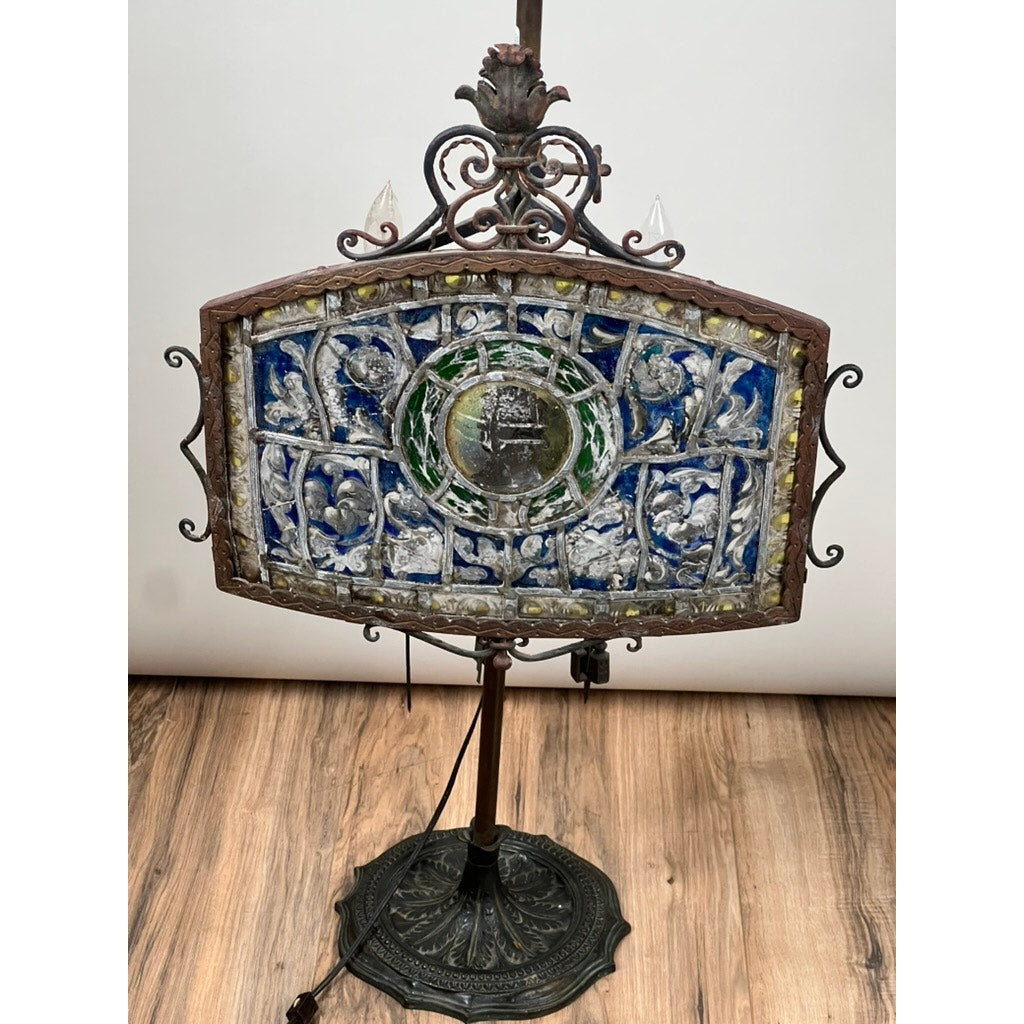 An Antique Five Burner Lucerne Whale Oil Lamp with a Napoleon I Fireplace Screen Shade, featuring ornate metalwork and intricate stained glass in blue, green, and clear, stands on a wooden floor. Brand: Unknown.