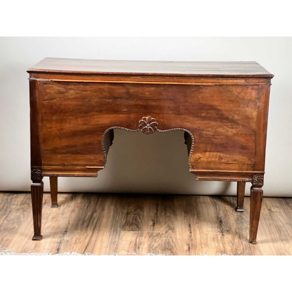 An Antique Louis XVI Period Ladies Desk with a tooled leather top (c. 18th century) stands on a wooden floor against a plain light wall, featuring curved front details, a carved floral accent, and four slender tapered legs.