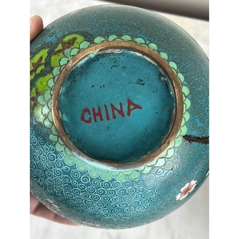 A close-up of the base of a Vintage Pair of Chinese Cloisonné Ginger Jars shows “CHINA” in red, with ornate swirling patterns and floral designs evoking Asian artistry. Visible wear around the base rim adds unique character. Brand: Unknown.