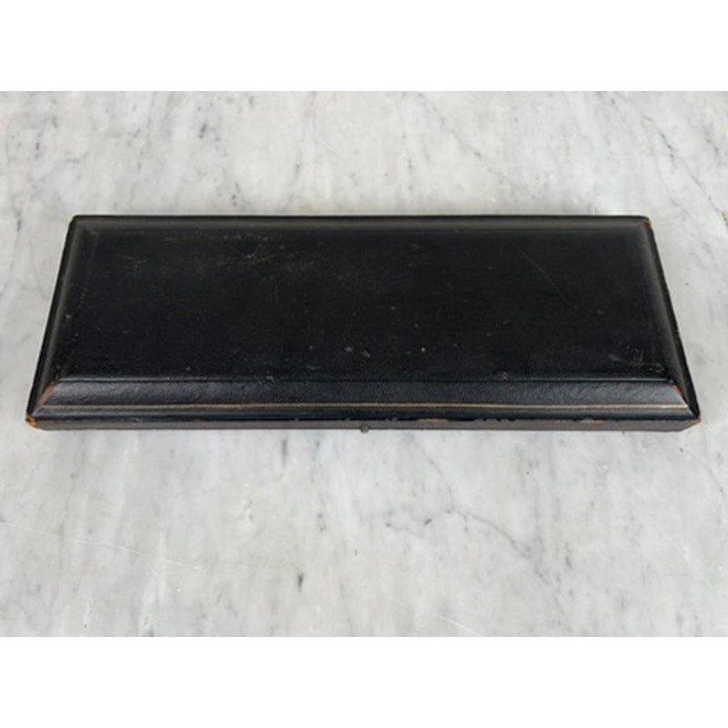 A rectangular black box, likely the original case for the Antique Victorian Silver-Plated Fish Serving Set (knife and fork), sits closed on gray marble, showing minor scuffs and scratches along its slightly raised lid. Brand unknown.