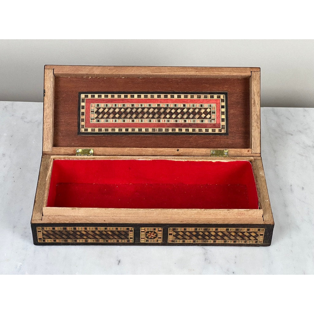 An Antique Persian (likely Syrian) Khatam Inlaid Wood Jewelry Box from the early 20th century, open to display its red velvet-lined interior, rests elegantly atop a marble surface.