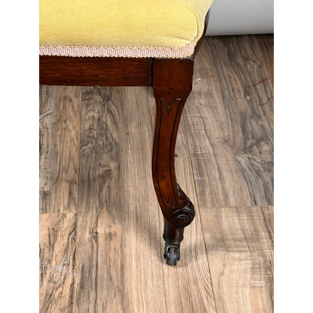 A close-up of a Fine Antique Renaissance Revival Walnut Side Chair (attr. John Jelliff, Newark c. 1880), showing its carved leg with a small wheel, yellow upholstery, and set on a wood-patterned floor.