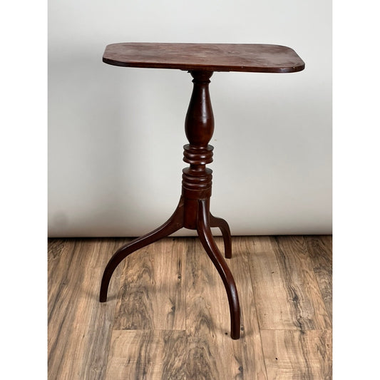 A compact, dark cherry Hepplewhite candle stand by Pearl City Antiques, featuring a rectangular top, turned central pedestal, and three gracefully curved legs, stands on a wooden floor against a plain white background—evoking the refined elegance of an Antique Federal Period Cherry Candle Stand from the mid-19th century.