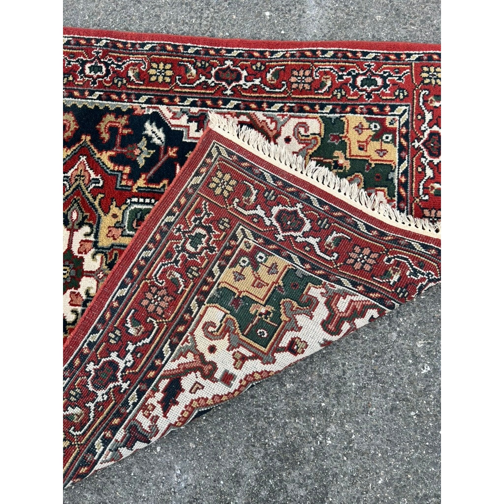 A Vintage Persian Heriz Hand Knotted Rug 4x6 with red, green, yellow, and black geometric designs is partially flipped to show its intricate weave as it rests on a rough gray stone surface. Brand: None and/or Unknown.