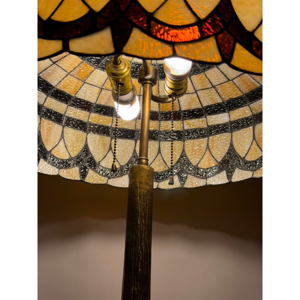 Close-up of the Vintage Tiffany Revival Leaded Stained Glass Table Lamp by Pearl City Antiques, showcasing its intricately patterned leaded stained glass shade with two exposed bulbs and pull chains, gracefully mounted on a cast brass tree-form base. Warm light glows through the vibrant glass design.