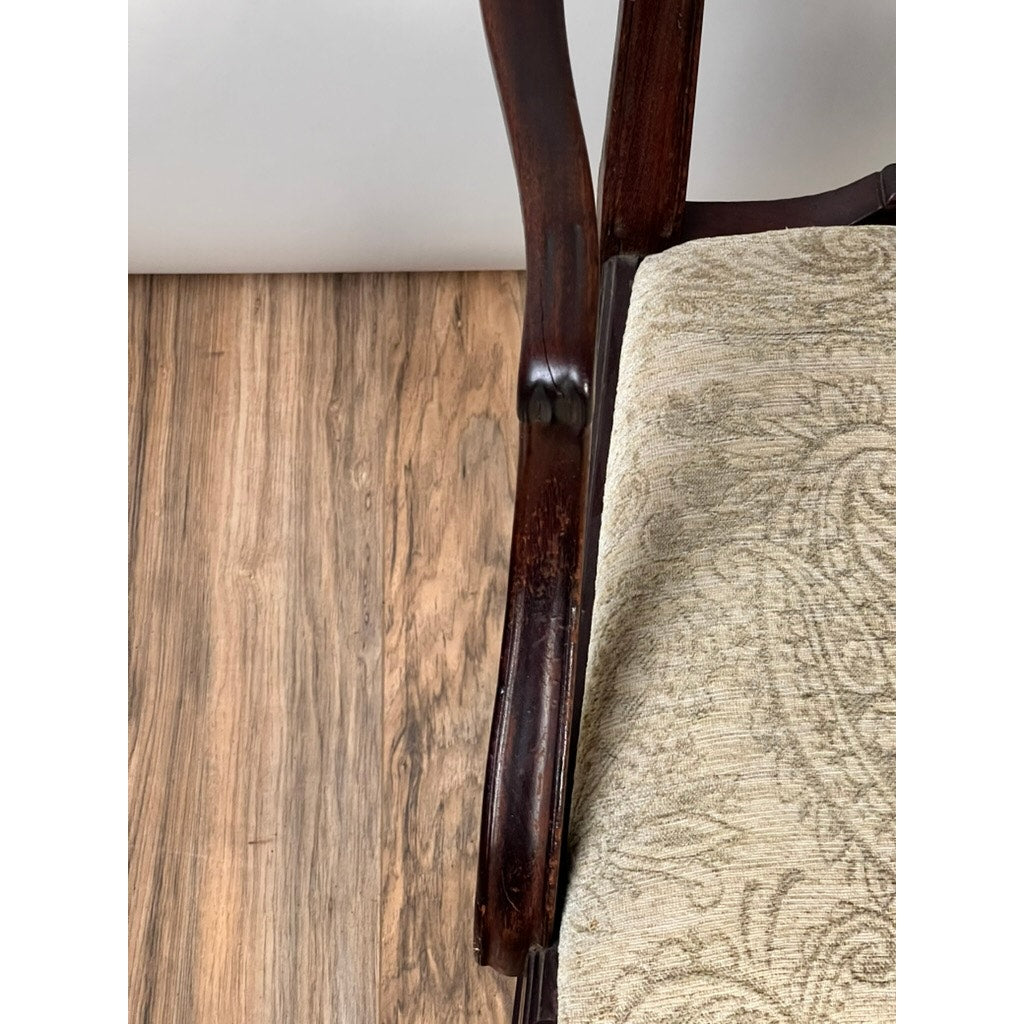 Close-up of an Antique English George III Mahogany Hepplewhite Armchair (early 19th century) with carved armrest and beige patterned upholstery, shown on a light natural wood floor. Brand: Unknown.