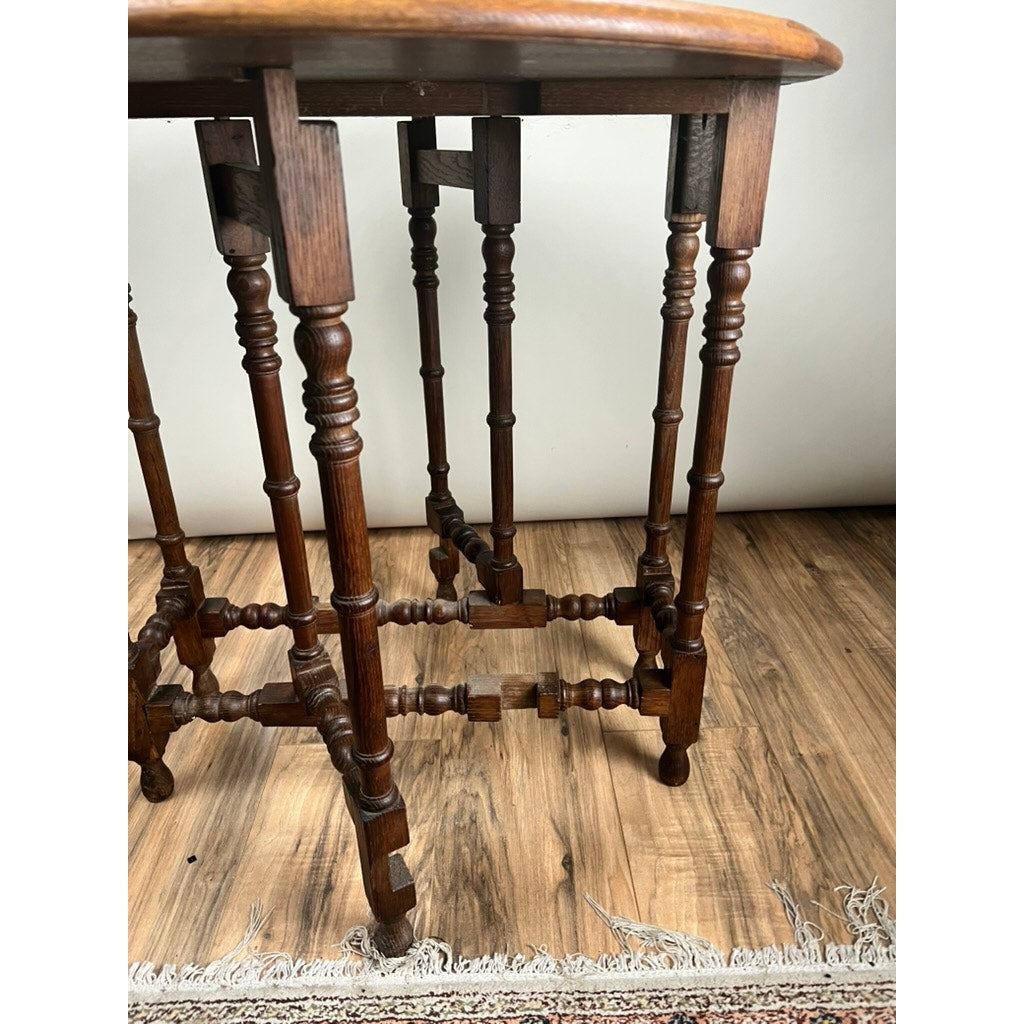 Close-up of ornately carved legs and crossbars from an Antique English Oak Carved Gateleg Occasional Table, late 19th century. The table rests on a hardwood floor with a fringed rug partially visible; the tabletop appears at the top.