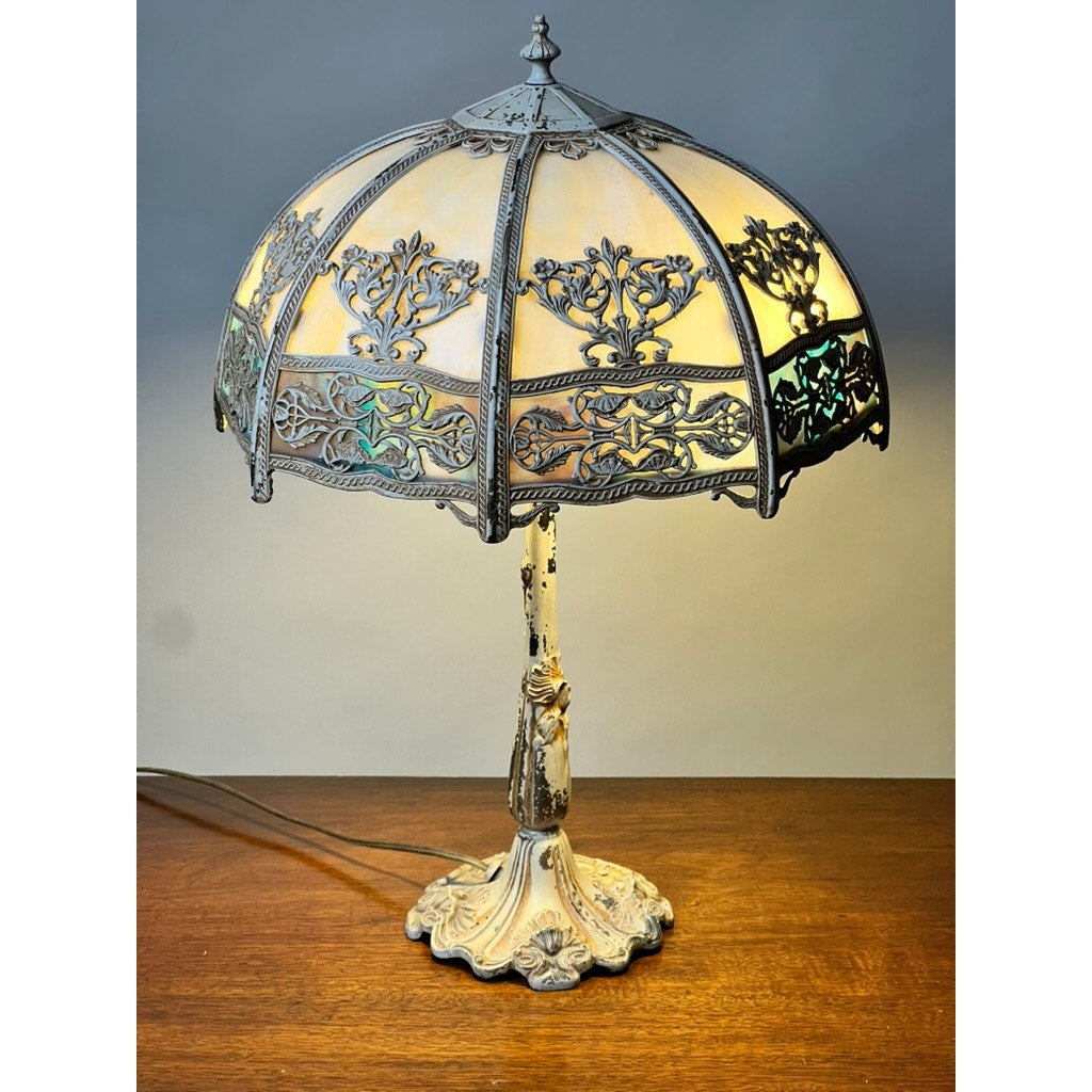 A Vintage Art Nouveau Slag Glass Two-Light Table Lamp (c. 1935–1955) with an intricate metal shade and glowing glass sits on a wooden surface against a plain background.