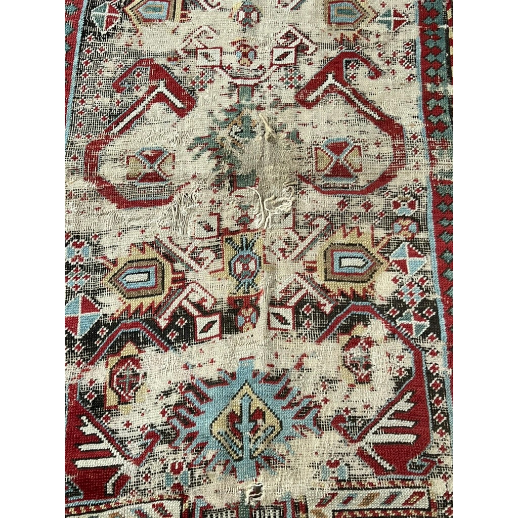 A detailed look at this Antique Caucasian Kazak Prayer Kilim (c. Mid 19th Century, 3’3” x 5’7”) showcases geometric rams’ horn motifs in red, blue, cream, and brown with visible center fraying and age wear.