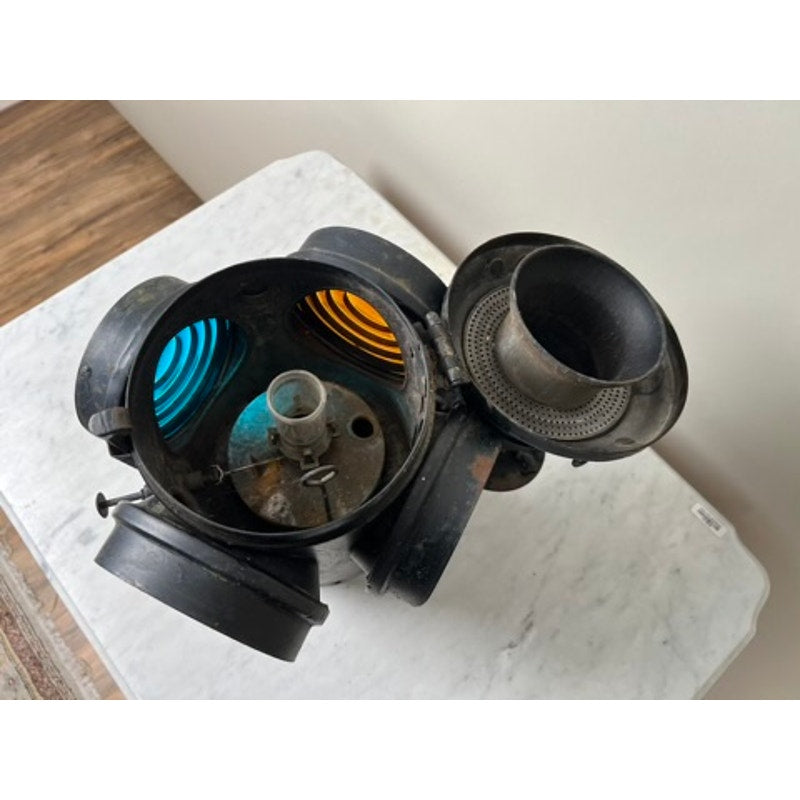 An Antique Illinois Central Railroad Signal Lantern by Dressel Arlington NJ, featuring blue and amber lenses and an open top, is displayed on a white marble surface with a wooden floor in the background.