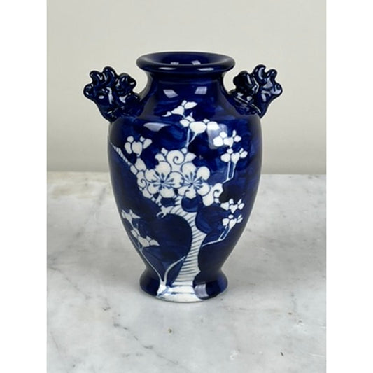 The Vintage Japanese Blue and White Floral Bud Vase by Pearl City Antiques is a deep blue ceramic piece inspired by classic blue-and-white pottery, adorned with delicate white blossom and tree motifs. Featuring two ornate handles shaped like tree branches on either side and displayed on a light marble surface, it stands as an exquisite example reminiscent of hand-painted Japanese ceramics.