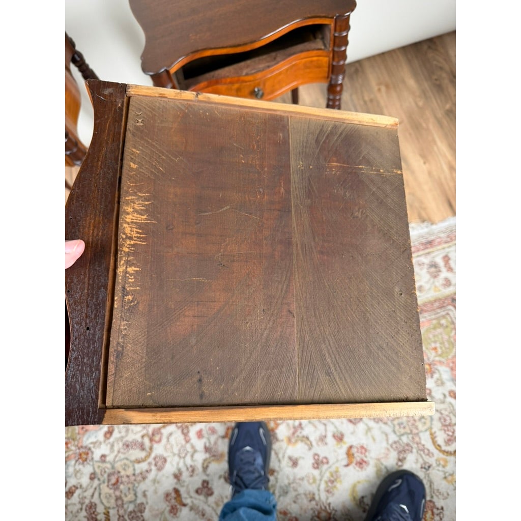 A hand holds the underside of a wooden drawer, with a matching Pair of American Classical Revival Mahogany Two-Drawer Work Tables, circa 1880–1910 visible in the background.