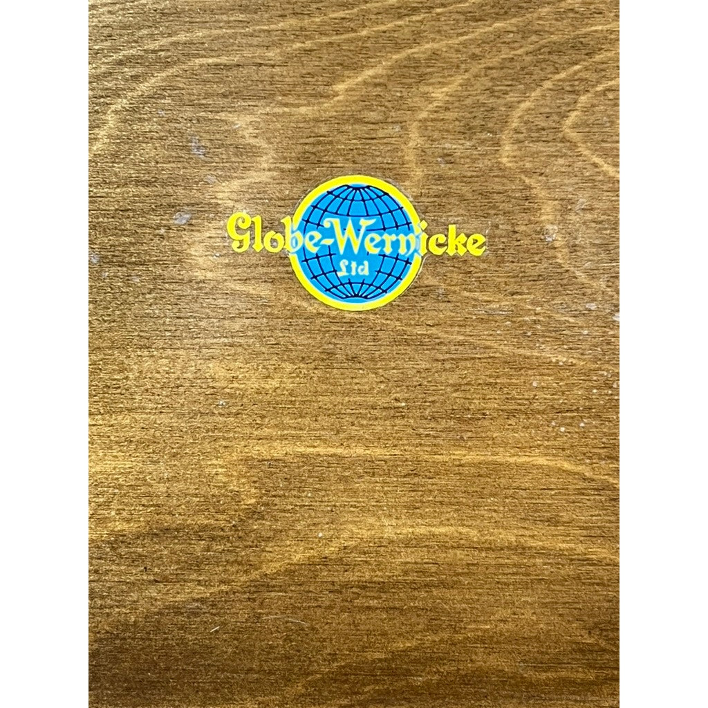 A vintage Globe Wernicke barrister bookcase features modular design, elegant leaded glass doors, and a wooden surface with a blue globe logo and yellow "Globe-Wernicke Ltd" text at the center.