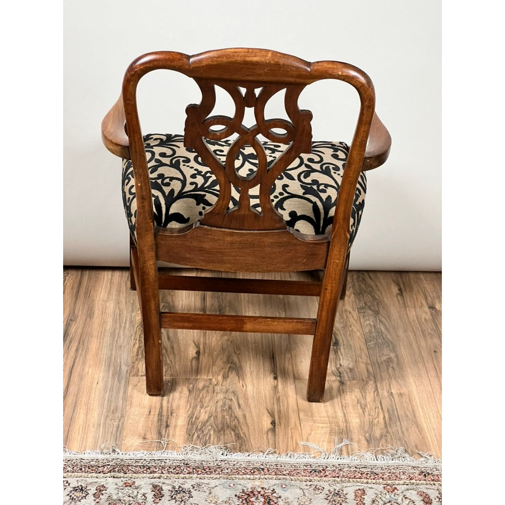 The Antique George III Chippendale Open Arm Chair (early 19th century) features an ornate backrest, curved armrests, and a black-and-white patterned cushion. It sits on a wooden floor beside a patterned rug. Brand unknown.