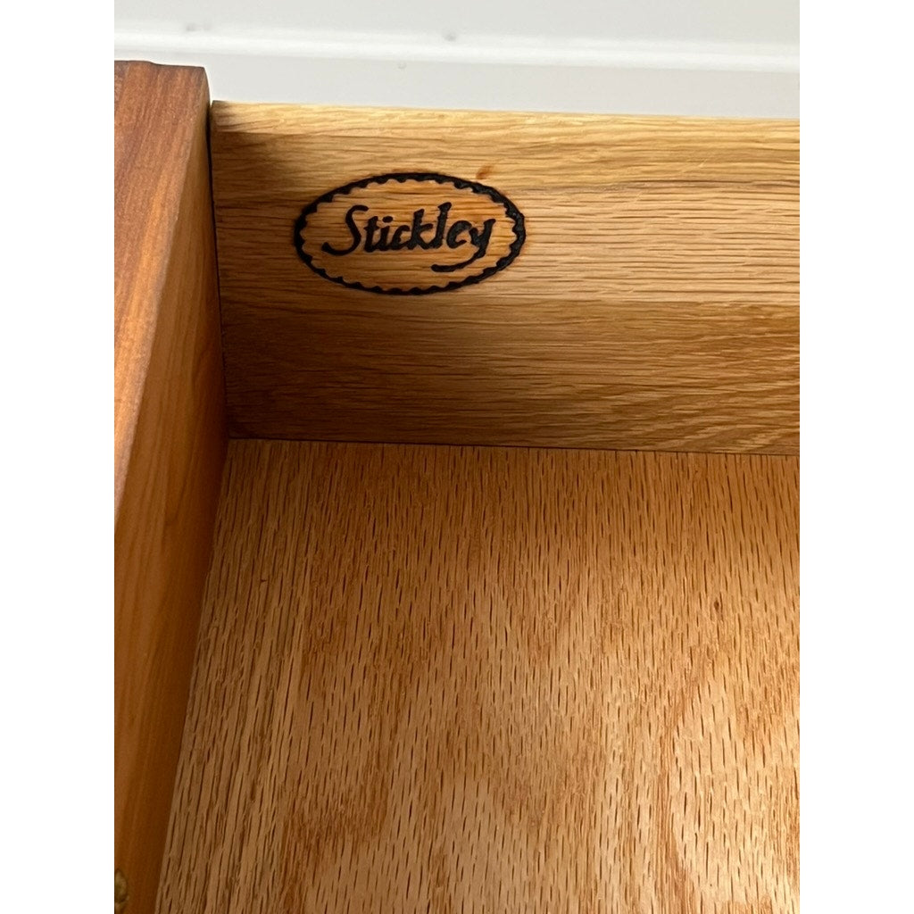Close-up of a drawer corner in the Vintage William IV Style Cherry Glass Door Bookcase by Stickley, featuring the Stickley logo stamped inside an oval. The smooth, light cherry finish highlights the wood grain and vintage glass panel doors complete the design.