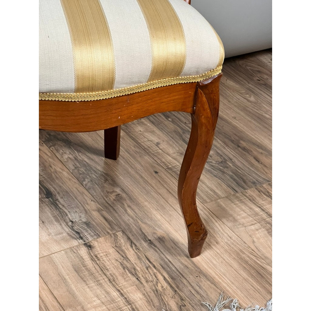 A close-up of a leg from a Pair of Antique Victorian Balloon Back Chairs (late 19th century), featuring a curved walnut design and beige with gold striped upholstery, shown on a wooden floor. Brand: Unknown.