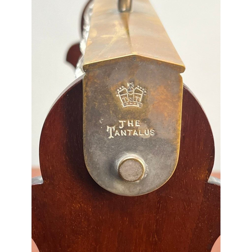 Close-up of an Antique English Edwardian Betjemann’s Cut Crystal Three Bottle Tantalus (early 20th c.) by Betjemann's, featuring a brass and wood frame, engraved crown, "THE TANTALUS" text, and central metal knob—ideal for displaying crystal decanters.