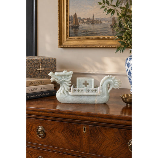 A light green celadon hardstone carving of a Chinese Carved Celadon Hardstone Dragon Boat with Figures & Fitted Box, featuring a central pavilion and resting on a wooden chest.