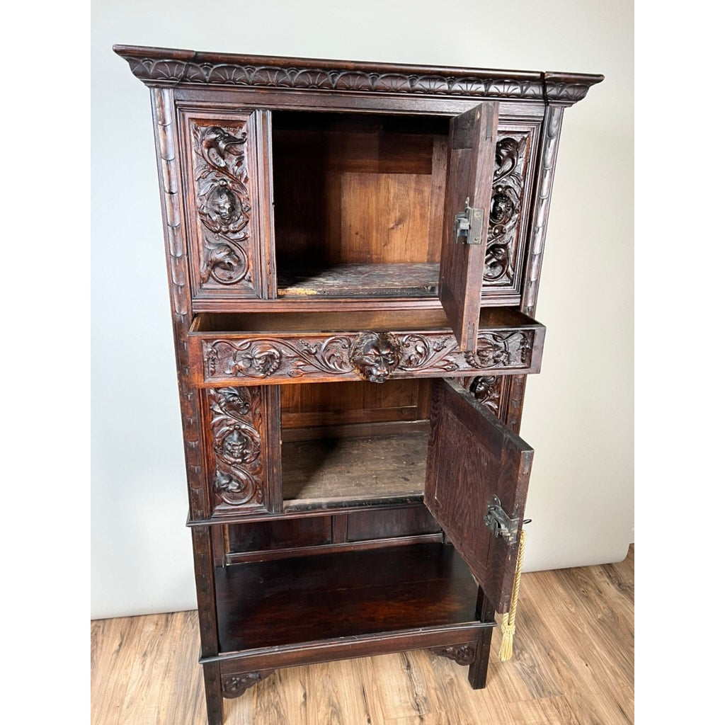 An Antique 19th-Century French Breton-Style Carved Oak Cabinet featuring deeply carved knights stands on a wood floor, its two open doors revealing empty compartments against a plain light-colored wall.