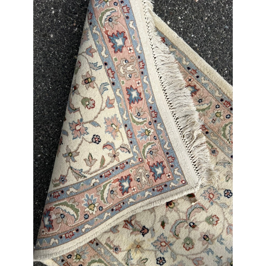 A close-up of a Vintage Nain Style Runner Rug with an ivory field (c. late 20th century, 2’6 x 23’9) shows floral and geometric patterns in pastel hues. A folded corner reveals its fringe and underside, displayed on a speckled surface.