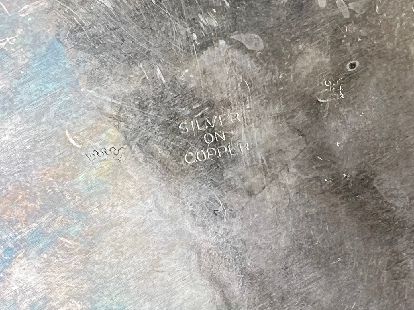 A close-up of the tarnished surface on the Pearl City Antiques Antique Silver on Copper Handled Serving Tray, showing engraved "SILVER ON COPPER" text amid scratches and marks.