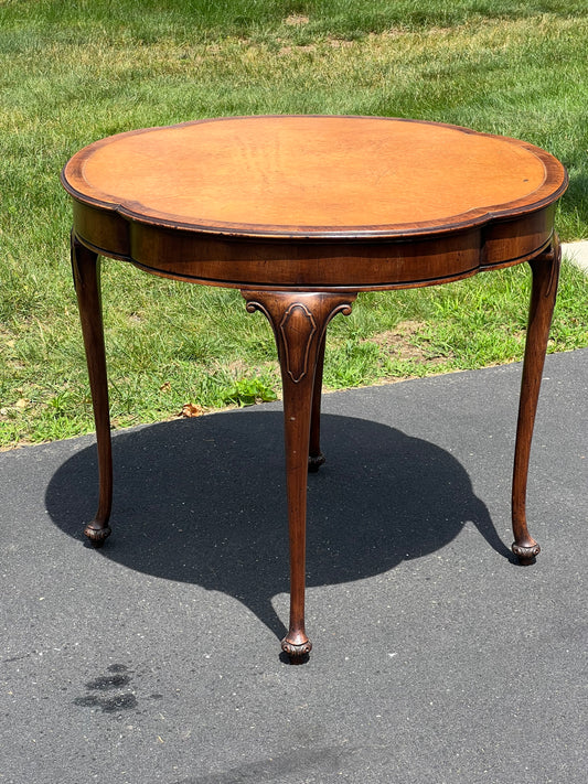 The Pearl City Antiques Antique Clover Shaped Queen Anne Mahogany Leather Top End Table stands on a paved surface, with green grass in the background under sunlight.