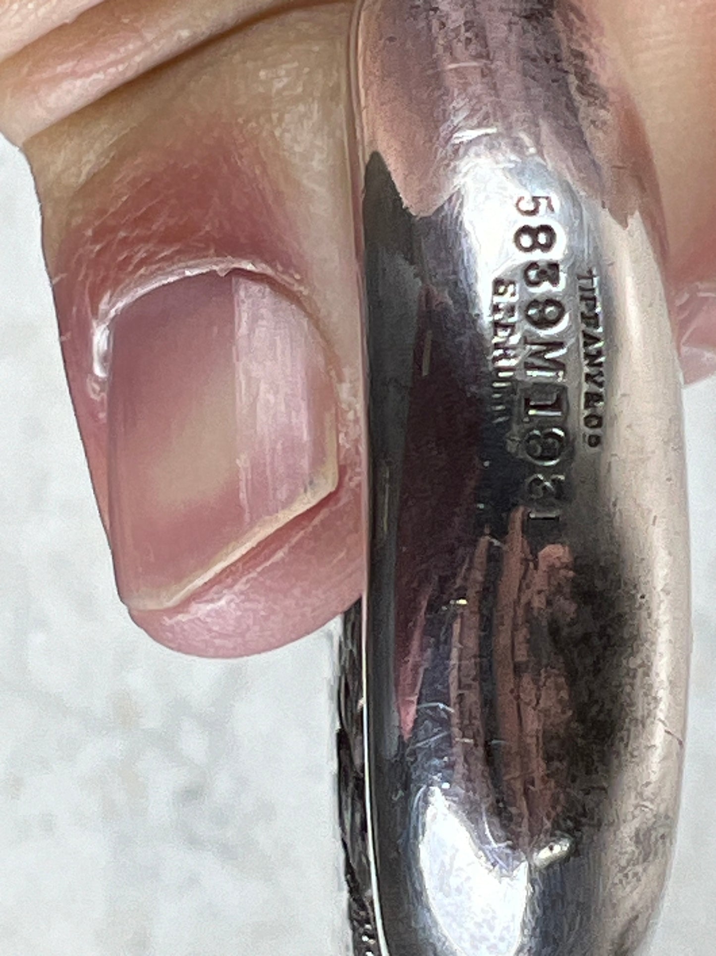 A close-up of a hand holding a detailed silver piece engraved with numbers, letters, 583, and Cyrillic—echoing the craftsmanship of the Depression Era Tiffany & Co Sterling Hand Mirror c.1931 from Pearl City Antiques.