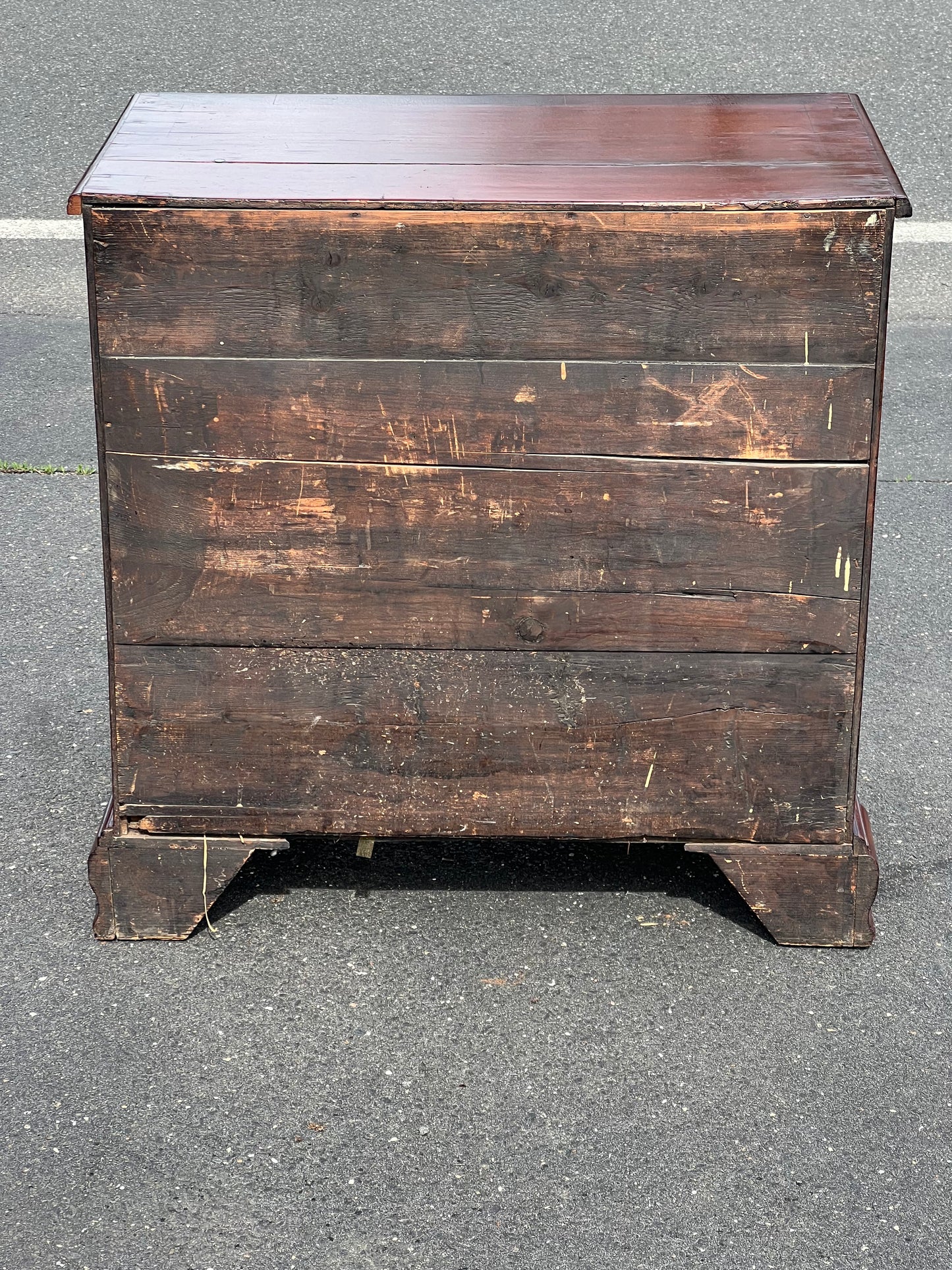 An Antique George III Mahogany Kneehole Desk from the late 18th century by Pearl City Antiques, featuring visible wear and discoloration, stands on asphalt pavement near a road.