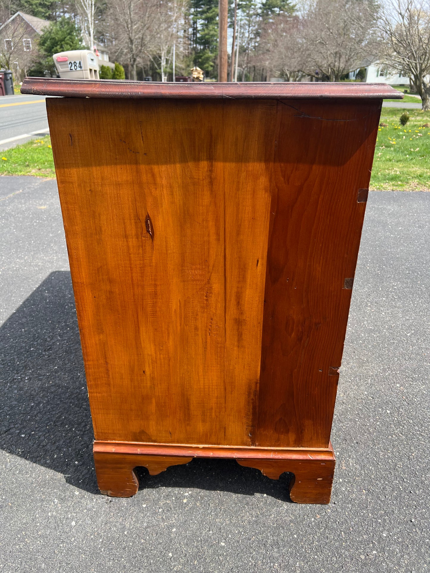 The Pearl City Antiques Antique Chippendale Pine Four Drawer Chest with Graduated Drawers, shown from the side on a driveway with trees and grass, is ideal for vintage home decor.