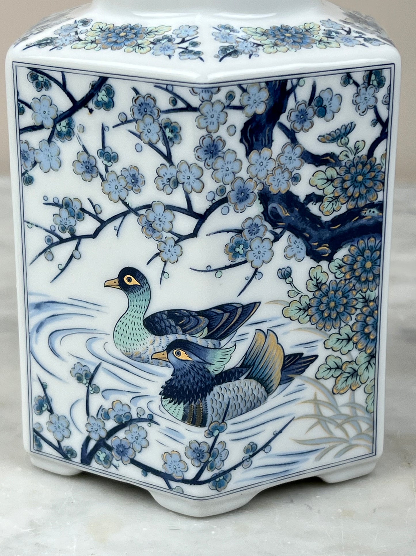 The Vintage Toyo Japanese Blue and White Porcelain Hexagonal Ginger Jar from Pearl City Antiques features detailed paintings of two ducks swimming among flowers and tree branches, with delicate green and yellow accents.