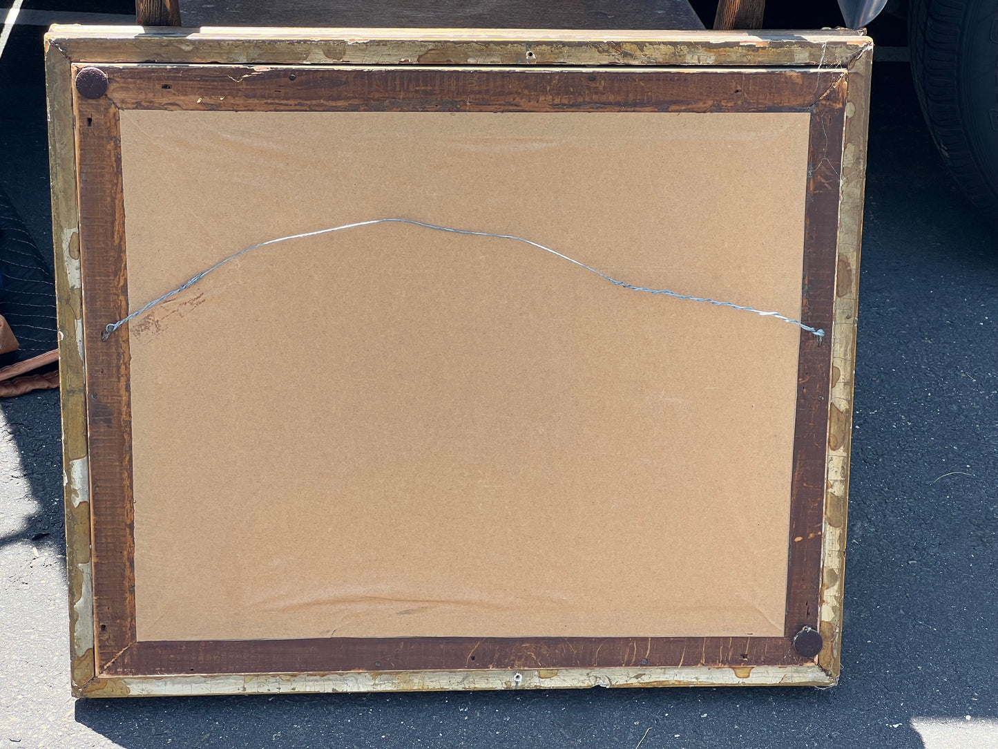 A back view of the Pearl City Antiques Vintage Gilt Wood Wall Mirror, featuring brown paper backing and a metal hanging wire, is shown resting outdoors.