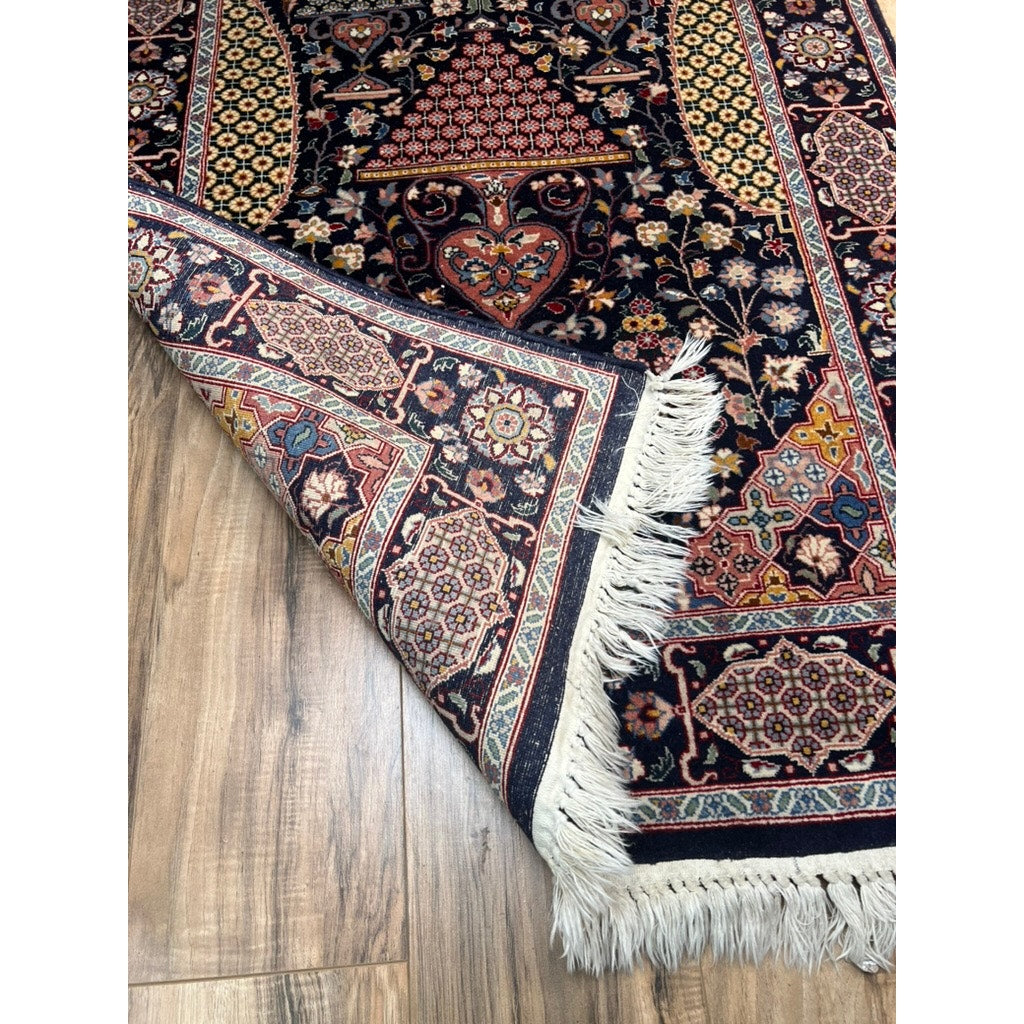 A Vintage Tribal Turkeman Hand Tied Wool Rug (3’1 x 5’) with intricate patterns and a fringed edge is displayed on a wooden floor, with one corner folded to show its ornate border.