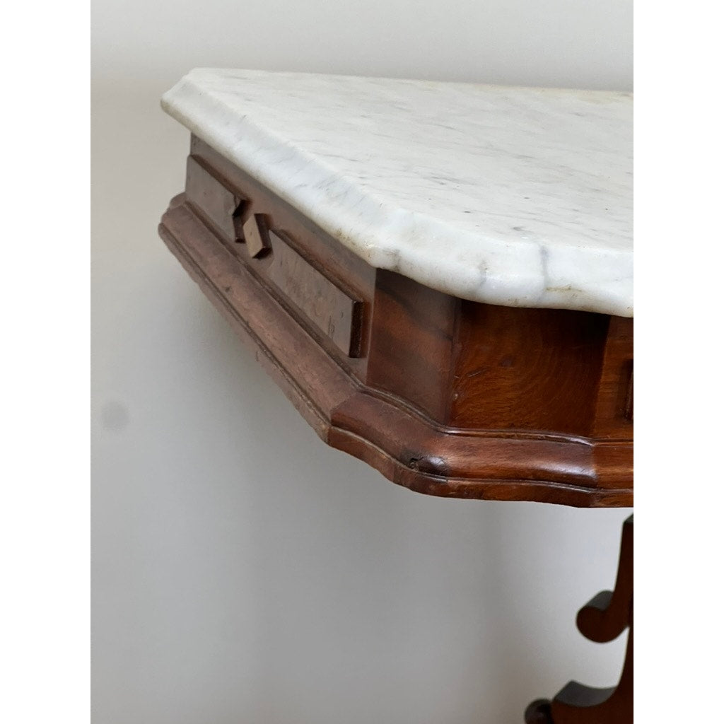 A close-up of the Antique Eastlake Victorian Walnut Marble Top Stand (late 19th century) highlights its decorative wooden trim and ornate leg, set against a plain, light-colored wall.