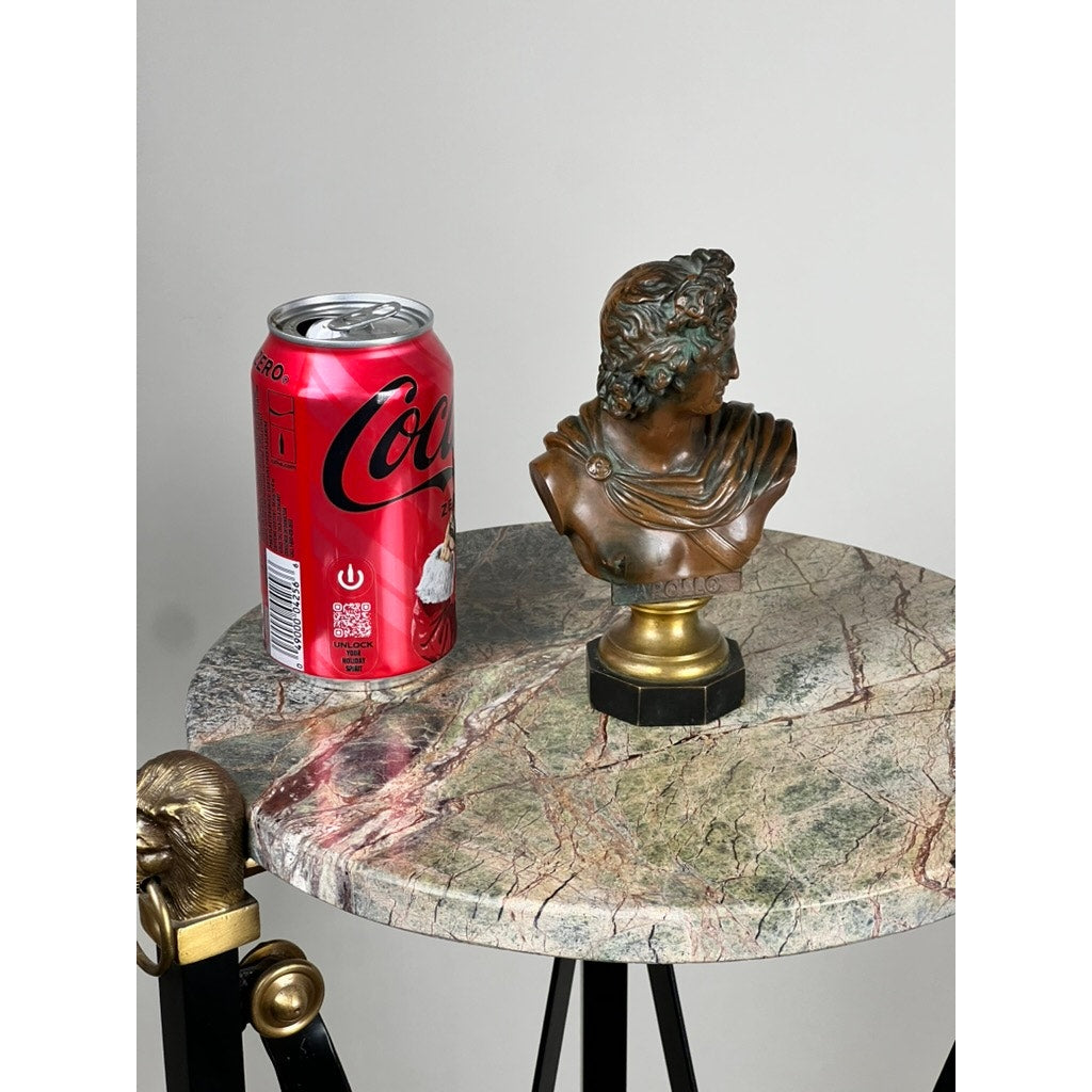 A red Coca-Cola can and an Antique Small Bronze of “the Apollo Belvedere” with Vienna Foundry Mark sit on a round, marble-topped table with patterned surface and black legs with gold accents, set against a plain light background.