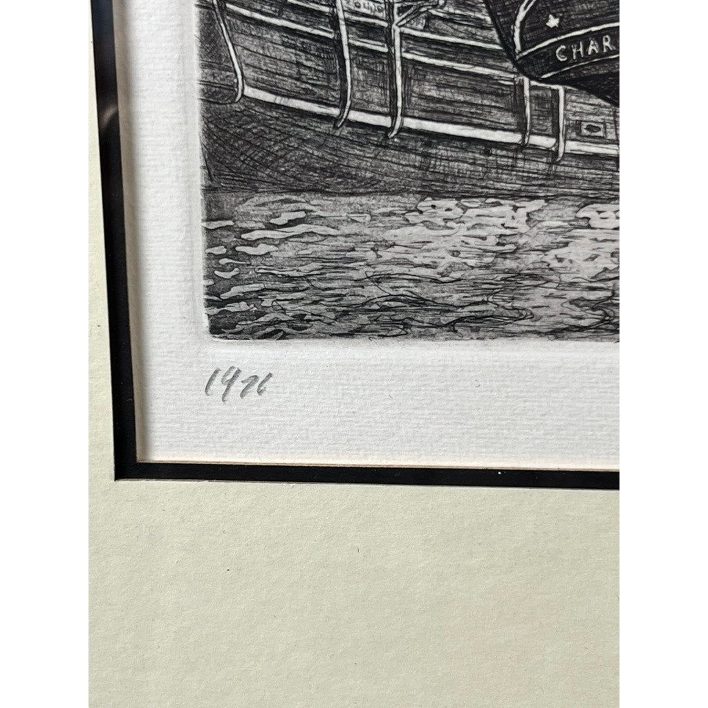A close-up of the bottom left corner of the framed etching “Whaling Ship Charles W. Morgan New Bedford” by Alan Jay Gaines shows part of a boat, water, and handwritten number 14/24—an evocative nod to American maritime history.