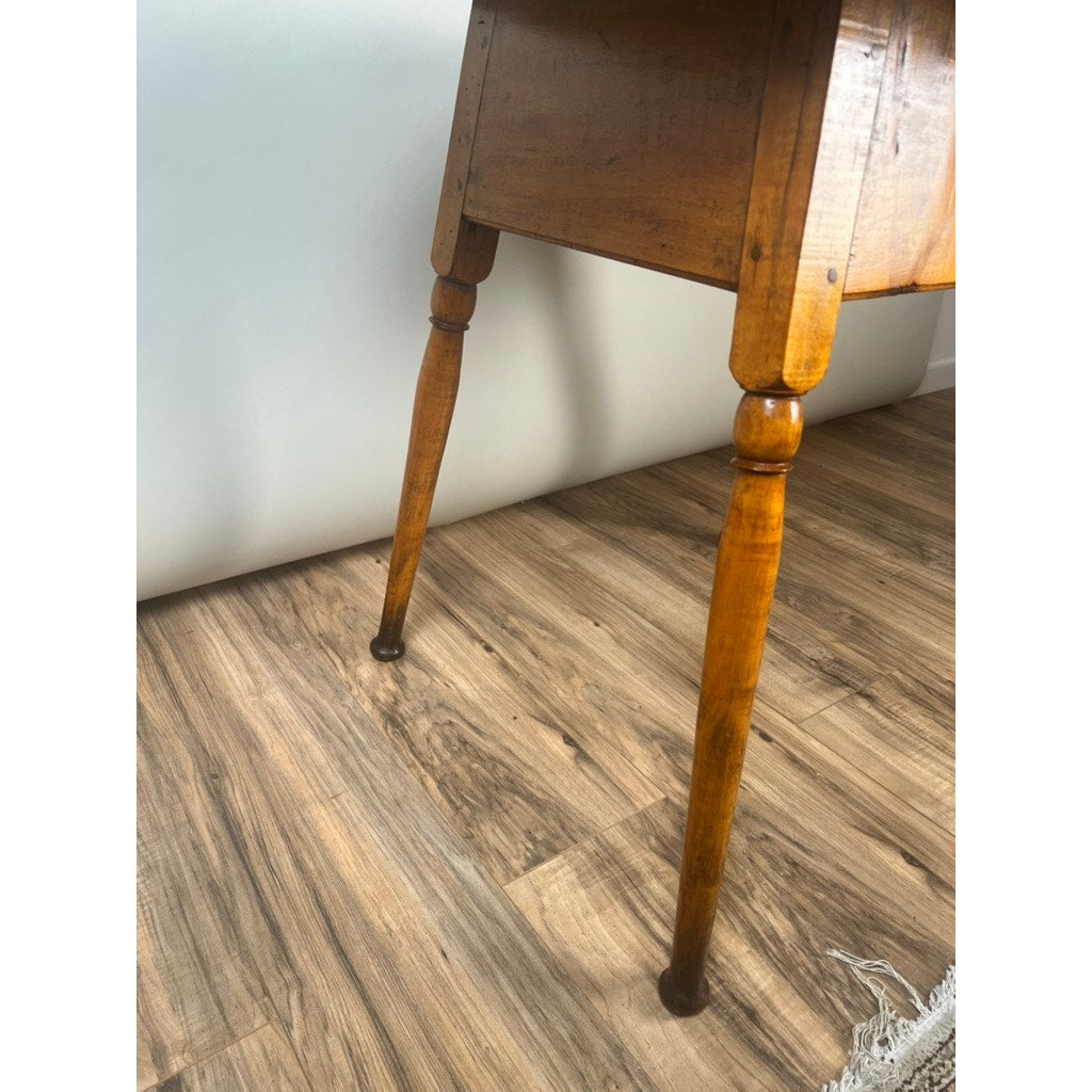 A close-up of the two wooden legs of an Antique American Queen Anne Maple Tavern Table, New England, circa 1760–1790, standing on a light brown wood floor with a white wall and a corner of a rug visible in the background.