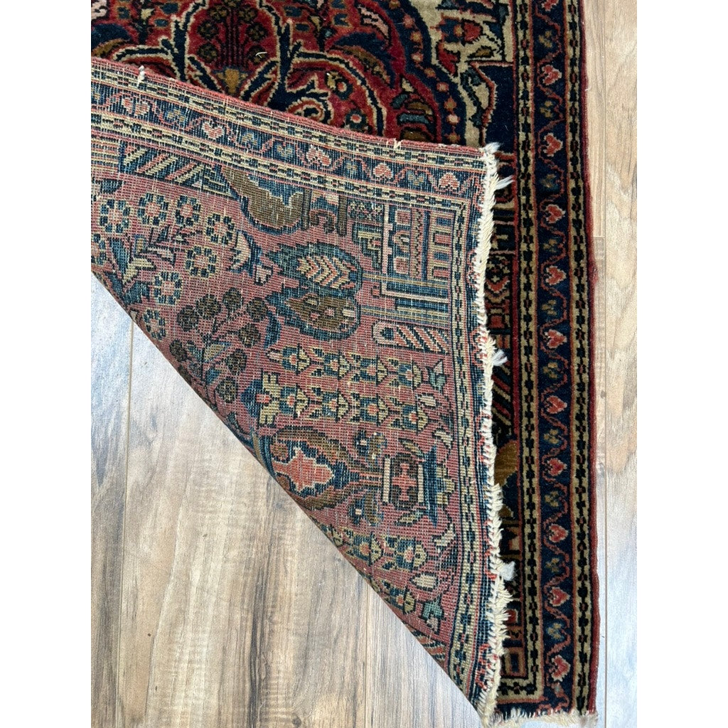 A corner of this Antique Persian Kerman Mat (c. Early 20th Century, 1’10 x 2’4) is flipped on a wooden floor, revealing intricate floral vase designs in muted tones on both sides. Brand: None/Unknown.