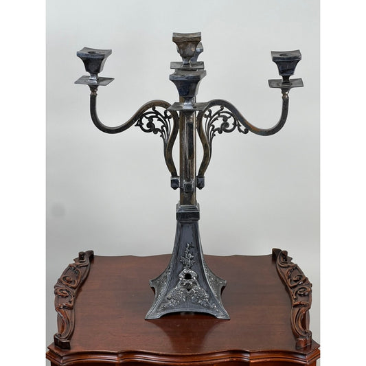 The Antique Art Nouveau Five Arm Candelabra by Poole Silver from Pearl City Antiques features ornate black scrollwork and floral detailing, with five candle holders, and is displayed on a polished wooden table with carved edges.