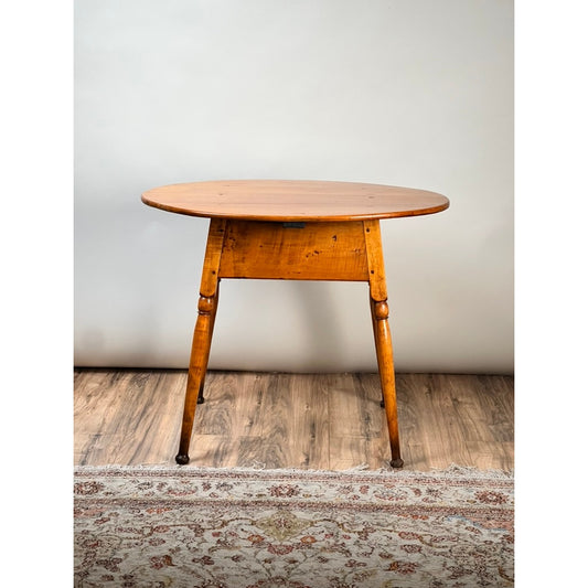 Certainly! Here’s a rewritten sentence using your product data: The Antique American Queen Anne Maple Tavern Table by Pearl City Antiques (New England, circa 1760–1790) stands on a wooden floor, partially atop a patterned rug and set against a plain light-colored wall, evoking the timeless elegance of New England furniture.