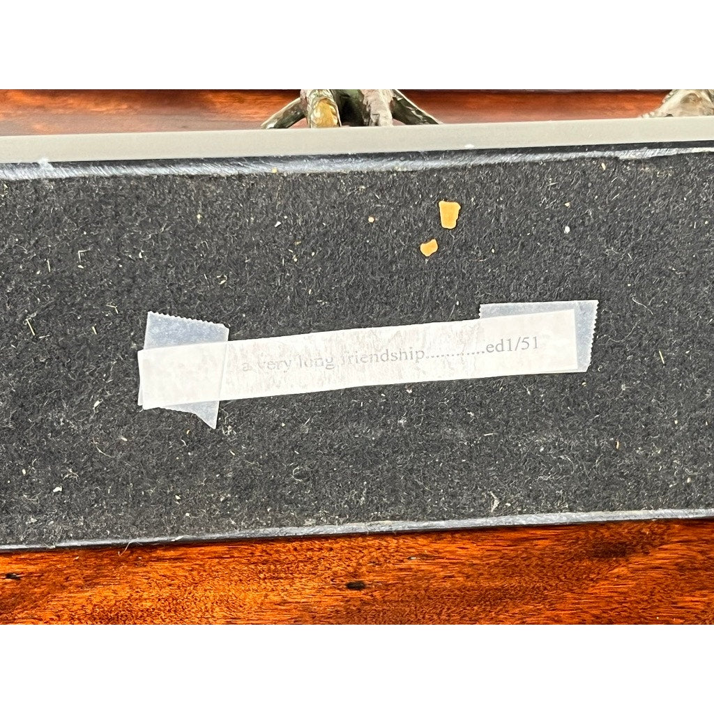 A strip of white tape with faded text reading “A very long friendship........ed 1/51” is attached to a dark surface beneath the Vintage Bronze Sculpture “A very long friendship” by Frank Califano, 1 of 51, resting on a wooden table.