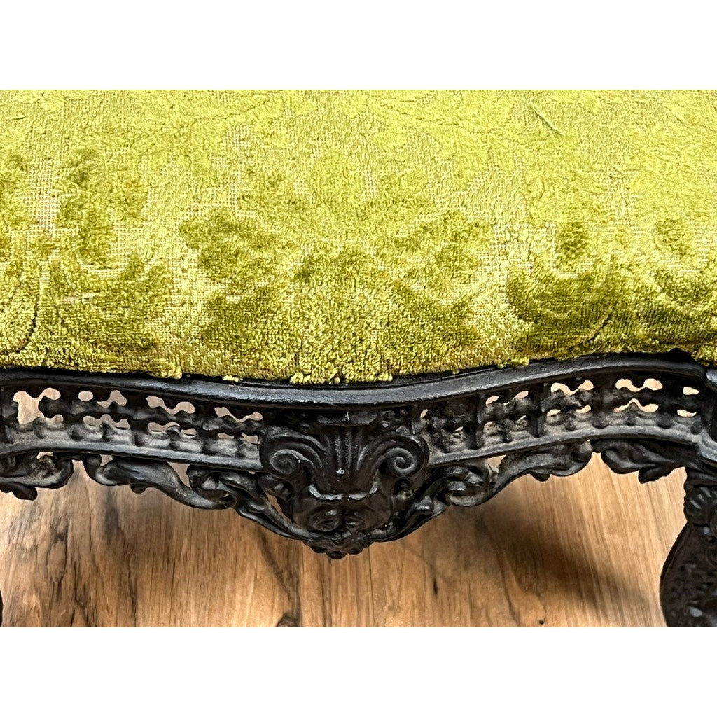 Close-up of an Antique Victorian Cast Iron Foot Stool c. 1900, featuring ornate cast iron design and a textured, golden-green cushion—an elegant decorative piece from an unknown maker, shown resting on a wooden floor.