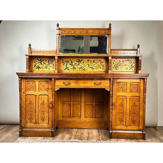 Antique Victorian Aesthetic Movement Oak Desk in Original Finish c. Late 19th Century by Pearl City Antiques, showcasing exquisite carved details, stained glass panels with floral motifs, a central mirror, drawers, and cupboards—evoking the elegance of Victorian-era craftsmanship—presented against a plain wall on a wooden floor.