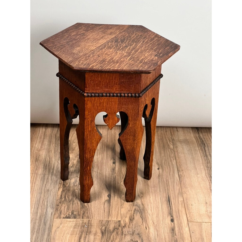 An Antique Arts & Crafts Small Oak Occasional Table c. 1910 with ornate cut-out legs, beaded trim under a hexagonal top, and warm brown finish is shown standing on a wood floor against a plain white background. Brand: Unknown.