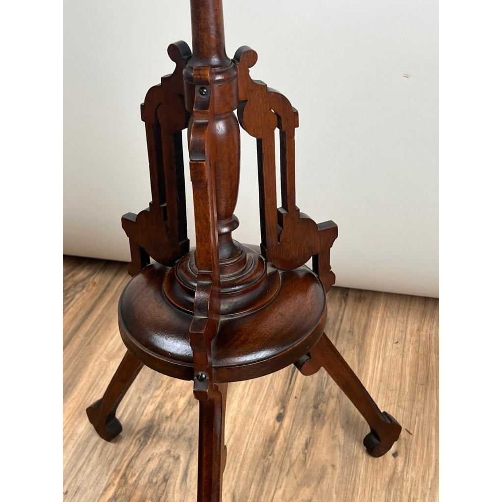 A close-up of the Antique Victorian Walnut Candle Stand (late 19th century), featuring elegantly carved legs and details, shown on a wood floor against a light, plain background. Brand: Unknown.
