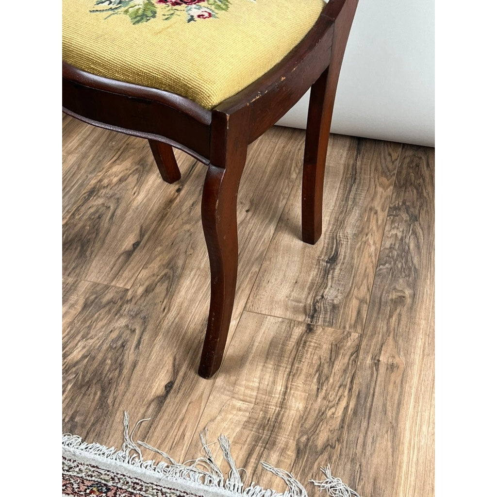 An Antique American Empire Flame Mahogany Saber Leg Side Chair (mid 19th century) with a yellow embroidered floral seat cushion stands on a wood-patterned floor beside the fringe of a patterned rug.